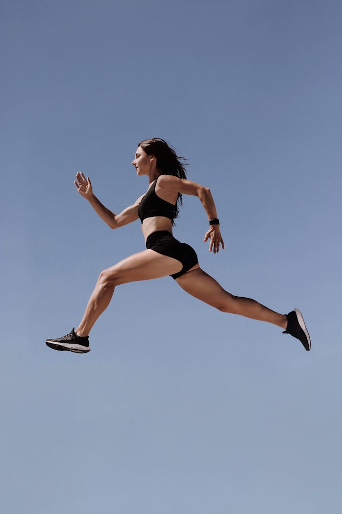 services-01 Energetic woman in athletic wear leaping against clear blue sky, symbolizing freedom and fitness.